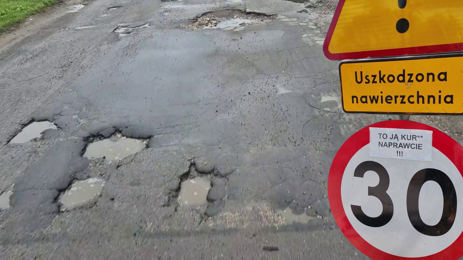 Dąbrowa Górnicza-Błędów. Ulica Zagórze. Dziurawa jezdnia i znak ostrzegawczy, z dopiskiem